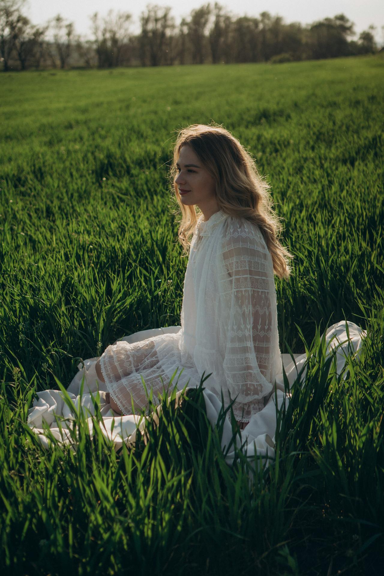 A Woman in White Dress Sitting on Green Grass Field